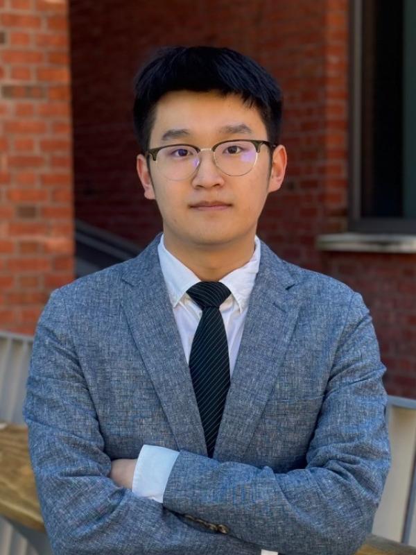 Forrest Lin stand with his arms crossed across his chest in front of a brick building.