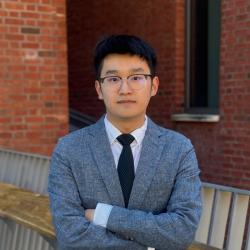 Forrest Lin stand with his arms crossed across his chest in front of a brick building.